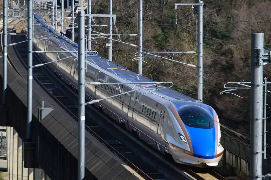 A white and blue high-speed train traveling beside a snowy railway